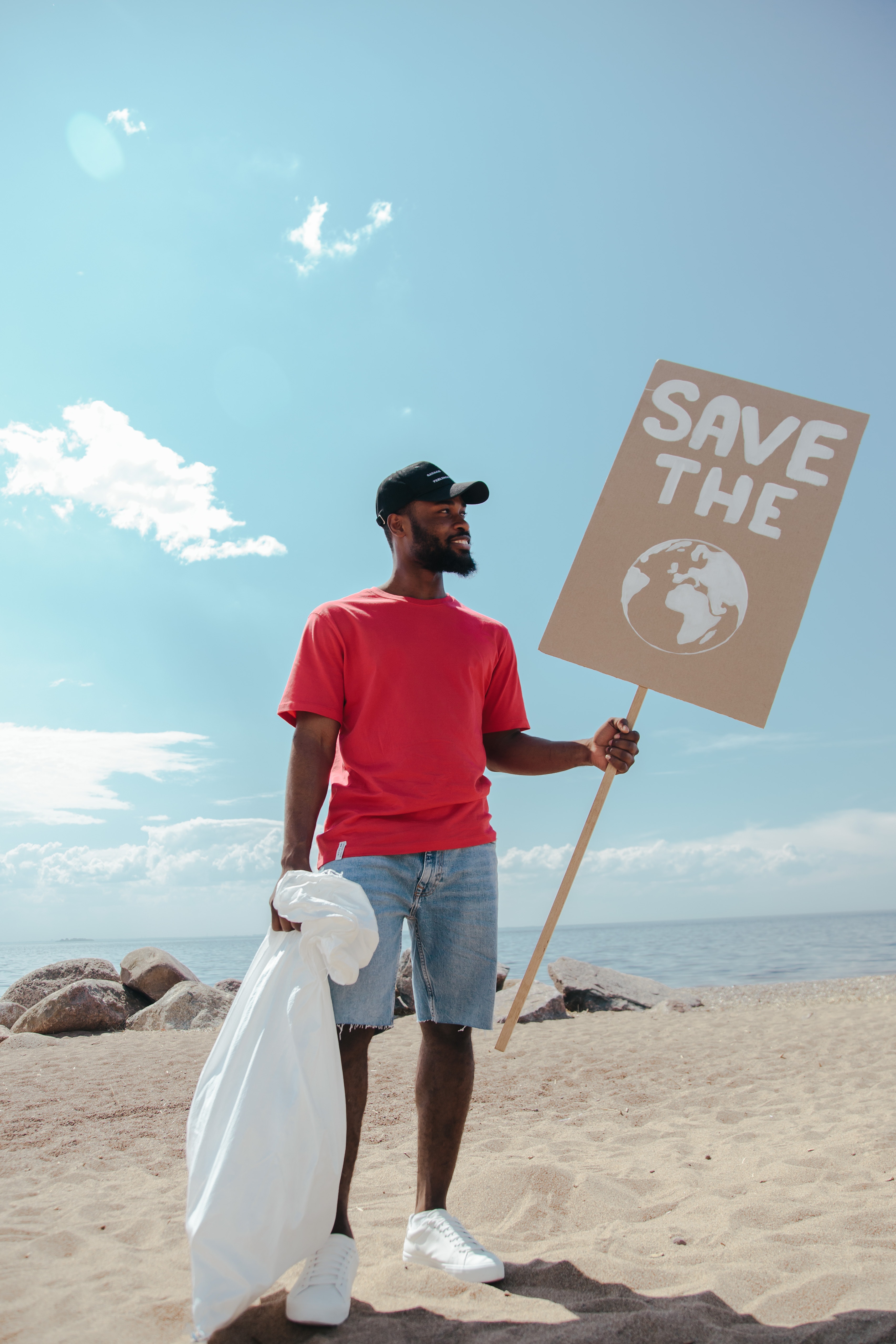 homme qui nettoie la plage des dechets et protections mentruelles jetables avec un sac poubelle et un paneau sauvez la planete