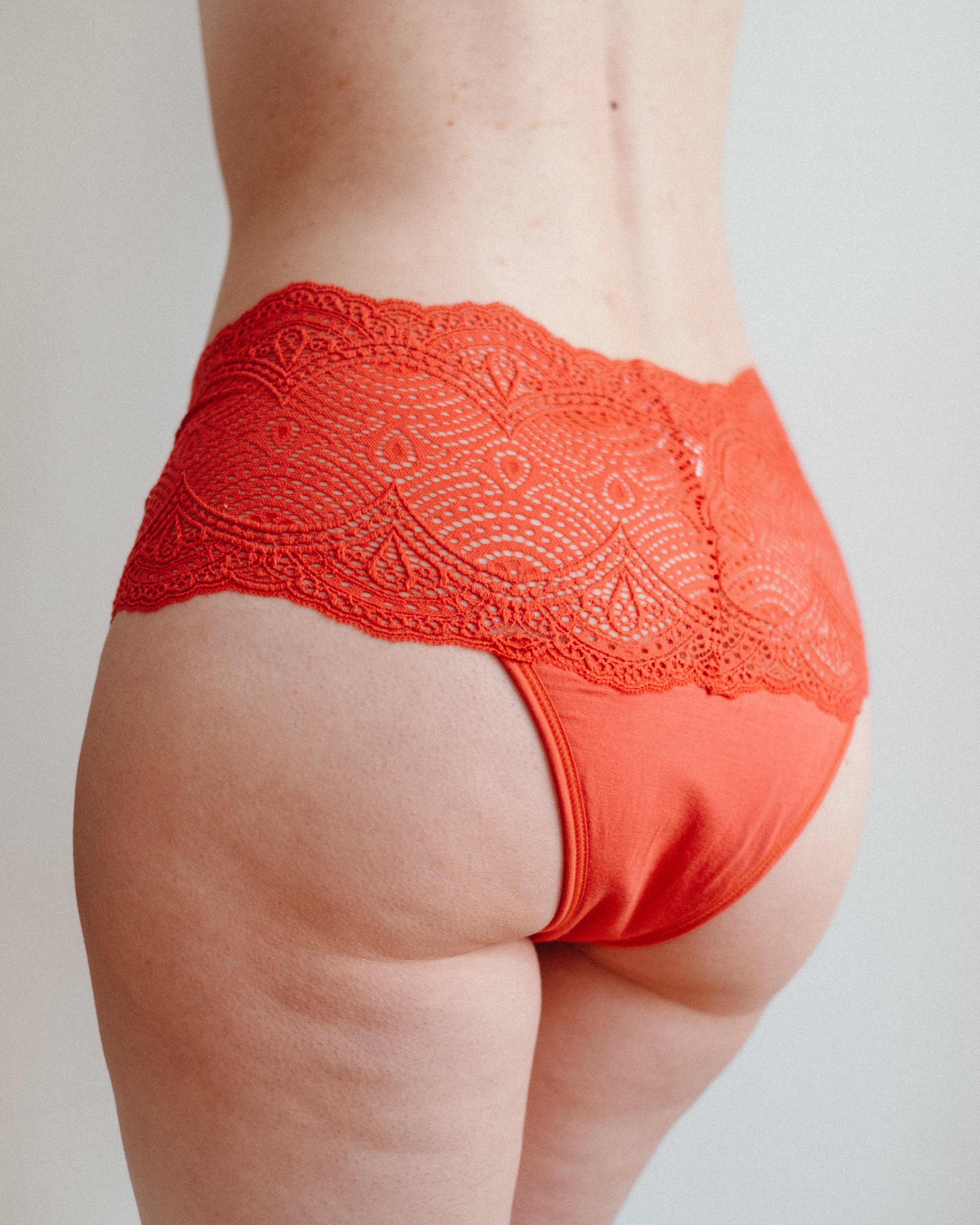 Femme de dos qui porte une culotte menstruelle en dentelle  rouge orangé