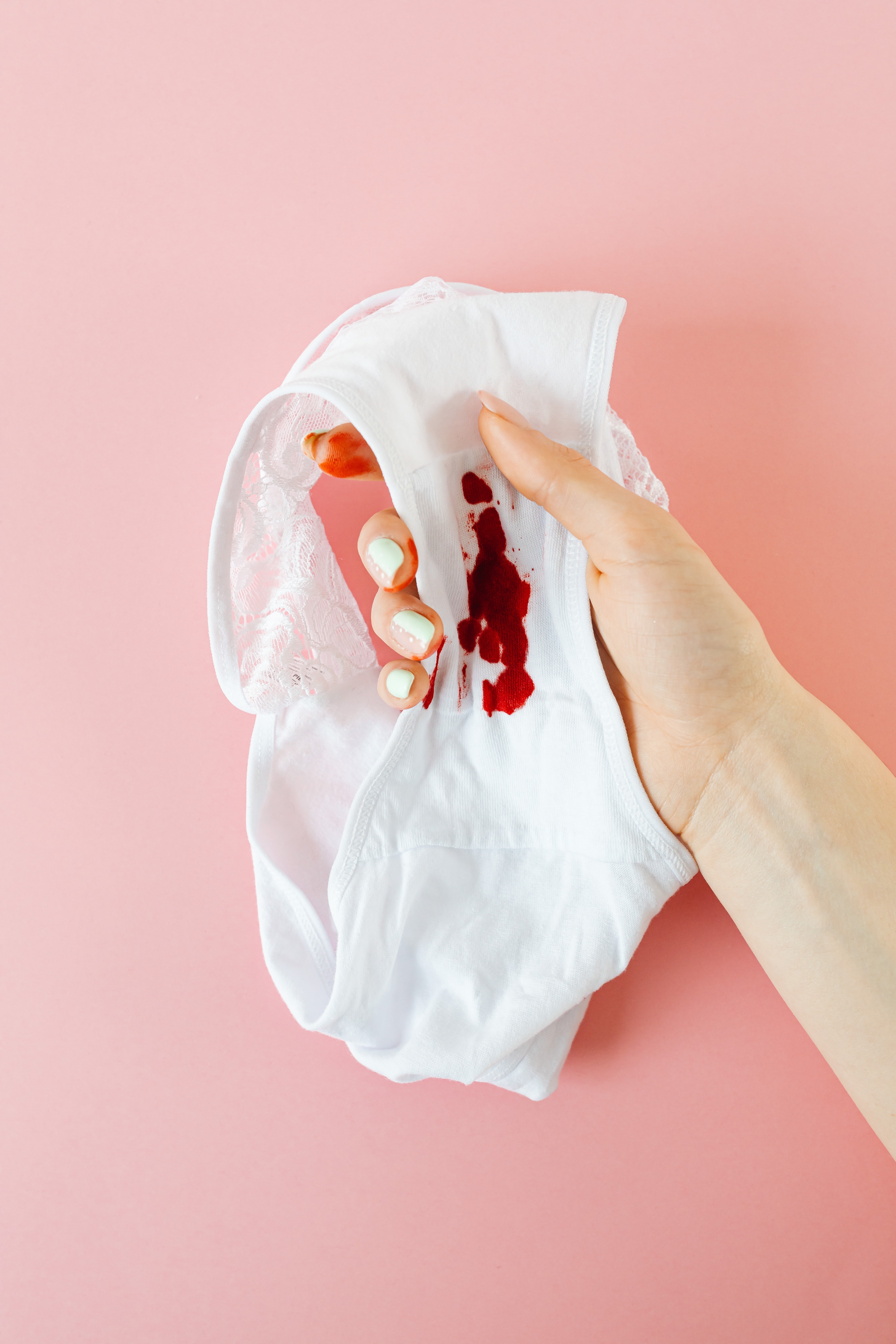 main d'une femme qui tient sa culotte avec des tâches de sang de règles car elle souffre de précarité menstruelle